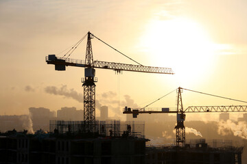 Silhouettes of construction cranes and unfinished residential building on sunrise background....
