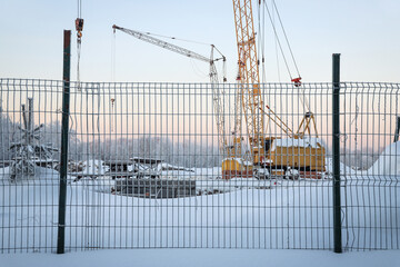 Construction behind a fence in cold winter against the background of frozen trees