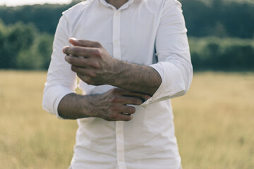 Sexy man buttons cuff-link on french cuffs sleeves luxury white shirt. Outdoor image. Summer background.