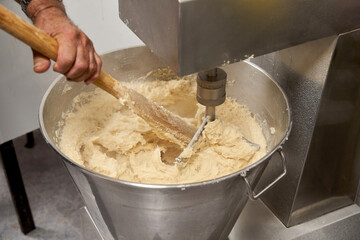 Close-up of a cook's hands stirring raw dough with a stick to make churros. Typical Spanish...