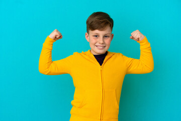 Little redhead boy isolated on blue background doing strong gesture