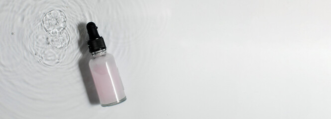 Small dropper bottle with pink cosmetic product on white surface with water. Copy space.