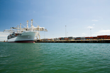 Naklejka premium Cargo ship moored in commercial harbor in Cape Town, South Africa, being loaded up with containers.