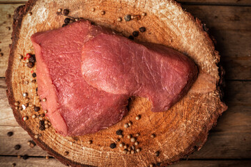 Raw game meat, beef, top view. Steaks, pieces of red meat on chopping block, wood slice. High quality roe, deer meat.