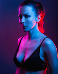 Stylish woman in colorful bright neon blue and purple lights. . Beautiful model posing in mystic smoke in the studio in black bra.