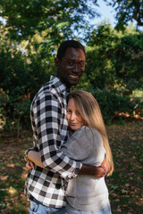 A couple of an African man and white woman are embracing and smiling in public green area