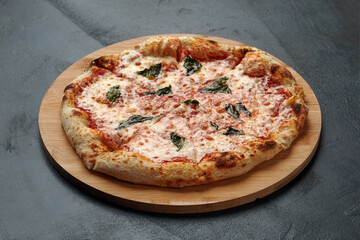 Uncut Italian pizza served with fresh basil leaf on Wooden board on dark texture background. Hot pizza with tomatoes and pesto sauce