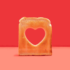 Minimal love concept. Arrangement made of one slice of toasted bread with a heart shaped hole in it. Red background.