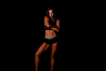 Beautiful athletic woman showing muscles on dark background. Slim tanned woman's body over black wall.