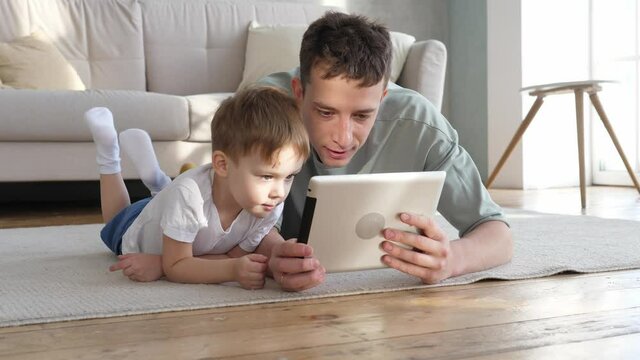 Happy father and cute preschool son using tablet watching cartoon enjoying watching funny social media video shopping online relaxing at home together