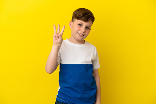 Little redhead boy isolated on yellow background happy and counting three with fingers