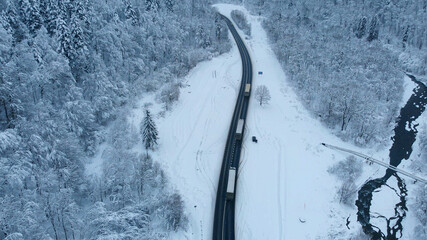 Aerial shot: Trucks driving by the road in winter forest.