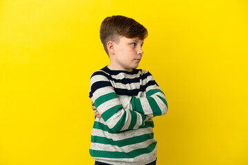 Little redhead boy isolated on yellow background keeping the arms crossed