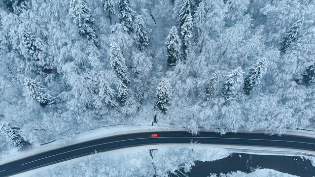 Aerial shot: Red Car driving by the road in winter forest.