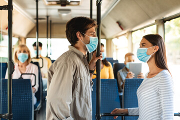 Naklejka premium Beautiful smiling couple in masks standing in bus and talking