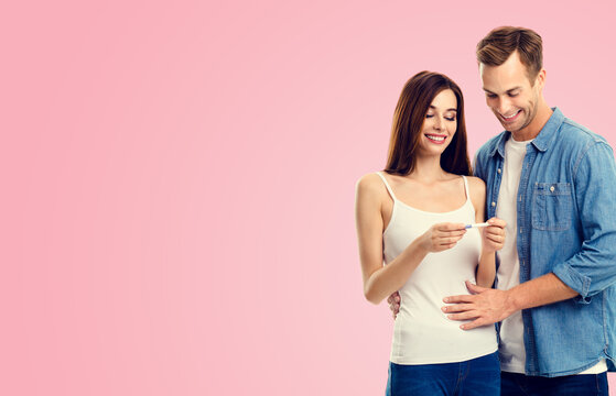 Love, relationship, new parents and happy family concept - young lovely couple, finding out results of a pregnancy test, isolated over pink color background.
