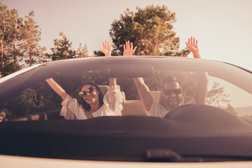 Photo of excited young couple have fun enjoy journey ride cabriolet arms up sunny weather weekend...