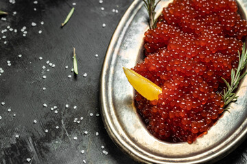 Red caviar in metal plate and a glass of champagne on a stone background. Gourmet food close up, appetizer, selective focus, place for text