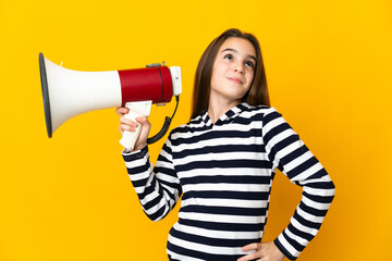 Naklejka premium Little girl isolated on yellow background holding a megaphone and thinking