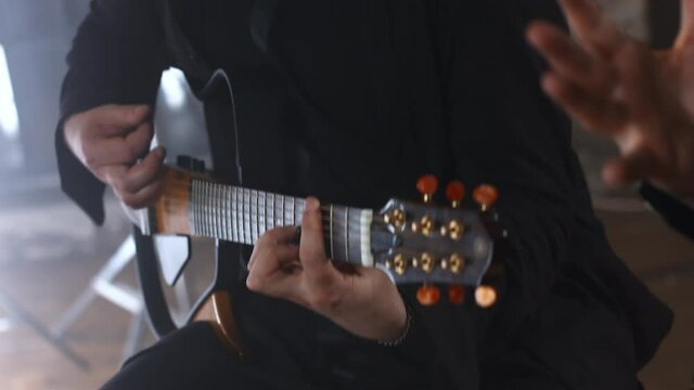 A European man in a black sweatshirt plays the acoustic guitar. Caucasian guy pinches a chord on the strings
