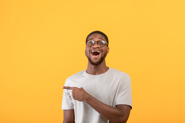 Surprised african american man pointing aside at blank space and looking at camera over yellow studio background