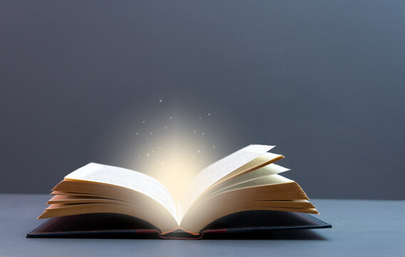Mystery open book with shining light . Fantasy book with magic light  and stars on a table with grey background  and copy space