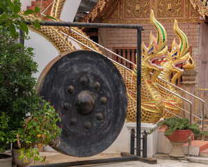 Big black gong hanging in metal frame with golden naga in background at historic ancient Wat Chiang...