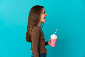 Little girl with strawberry milkshake isolated on blue background laughing in lateral position