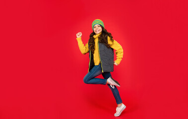 full length of jumping kid with curly hair in hat. teen girl on red background.
