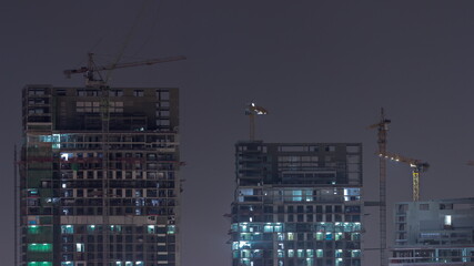 Fototapeta na wymiar Tall buildings under construction and cranes night timelapse