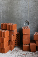 stack of red lightweight clay bricks against a concrete wall. Construction site. Environmentally friendly materials for the construction of load-bearing and dividing walls.