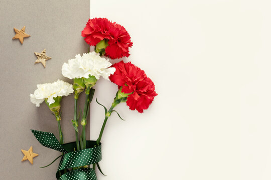 Mans Day holiday card with red and white carnations with gift ribbon and wooden stars on a green background with copy space for congratulatory text suitable for 23 february, 9 may or fathers Day