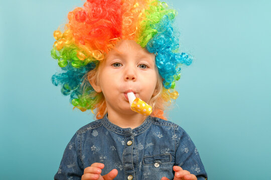 A little girl in a clown wig blows a festive air whistle.