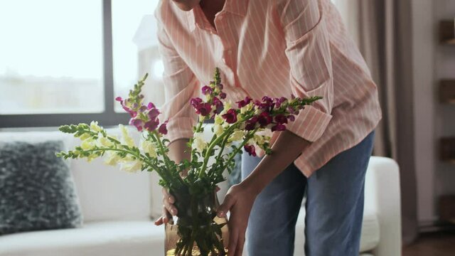 household, home improvement and interior concept - young woman placing flowers on coffee table