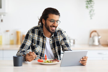 Handsome arab guy having breakfast, using digital tablet, copy space