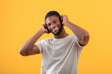 Fototapeta na wymiar Portrait of positive african american man listening music in wireless headphones, posing over yellow background