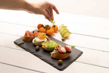 Making sandwiches, preparing crostini, canape, antipasti with salmon avocado, tomatoes, cream cheese, mozzarella for party ,birthday . The concept of healthy food and mediterranean cuisine.