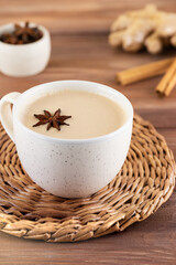 Masala tea with milk, anise and spices in a mug on a wooden table.
