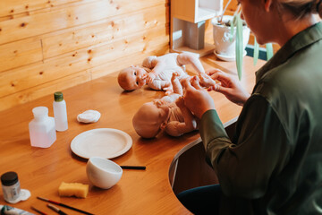 Reborning, handmade newborn baby doll, hobby, craft concept. Young female craftsman sitting with...