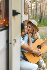 An Asian couple in love travel on a camper on their honeymoon after the wedding in an adventure forest in nature in the summer. A man sings a romantic serenade to a woman on a guitar on a road trip