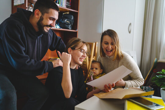 Group of people young woman caucasian female student sitting at home with her friends and family holding envelope with mail letter happy exited smiling reading entry test results success concept