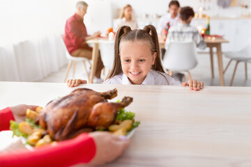 Cheery little girl looking at roasted Thanksgiving or Christmas turkey, cannot wait for holiday...