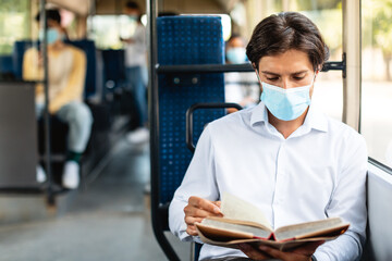 Focused man in mask reading book sitting at autobus © Prostock-studio