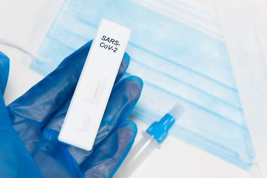 Concept of antigen test for the COVIC-19 coronavirus. The doctor's hands with blue gloves holding the test waiting for the result, white table with blue surgical mask and tube with diluent.