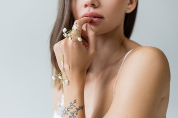 cropped view of young woman with tiny flowers on tattooed hand isolated on grey.