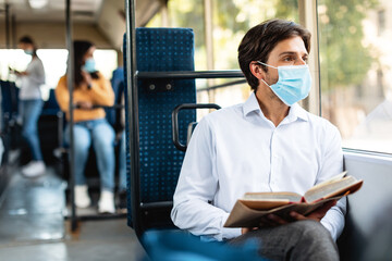 Pensive man in mask reading book sitting at bus