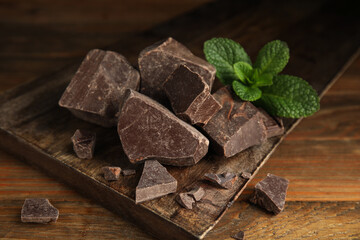 Tasty dark chocolate pieces with mint on wooden table