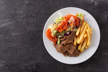 Plate of kebab, vegetables and french fries on black background