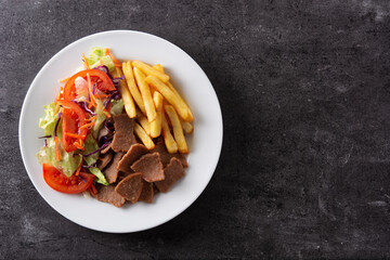 Plate of kebab, vegetables and french fries on black background