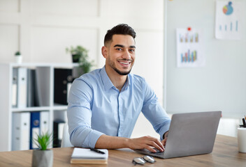 Attractive young Arab businessman using laptop pc at his desk in home office